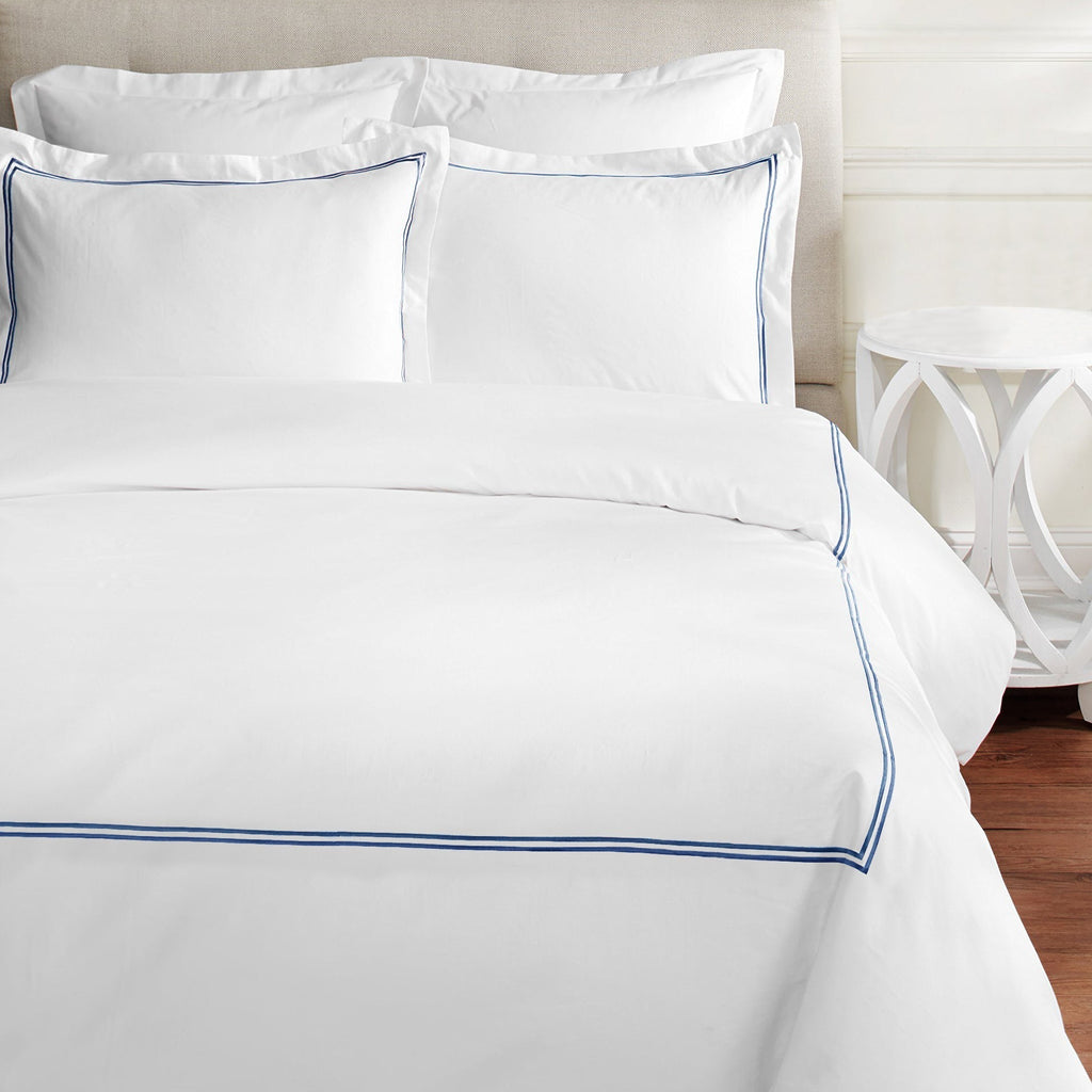 White bedding set with blue piping on a bed in a bedroom setting - The Well Appointed House