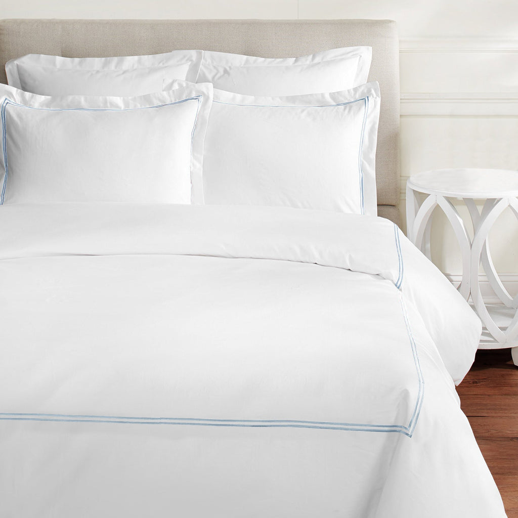 White bed sheets with blue piping on a bed in a bedroom setting - The Well Appointed House