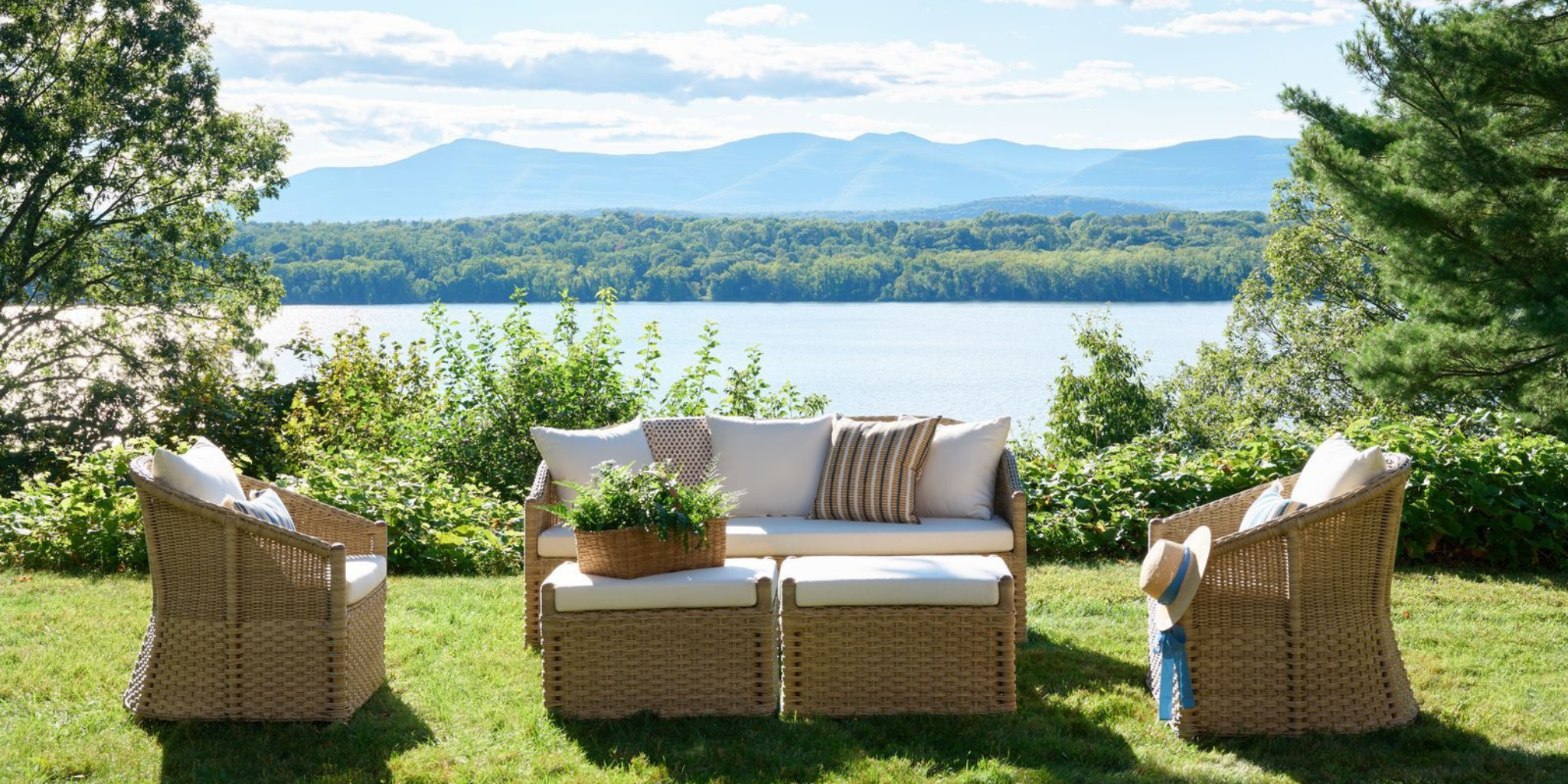 Outdoor patio set with cushions and a plant, overlooking a lake and mountains.